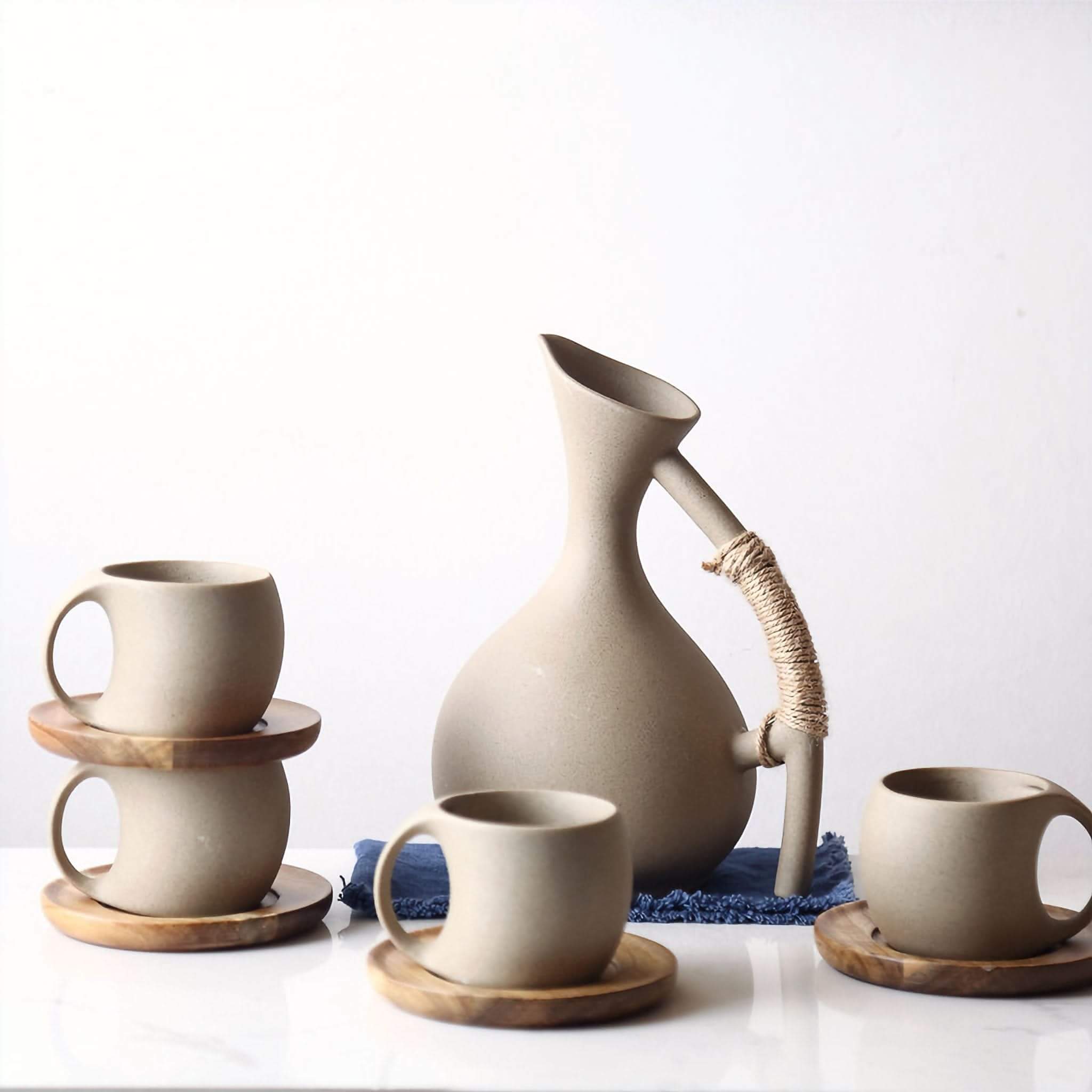 Set of 3 beige abstract ceramic mugs with arched handles on wooden coasters